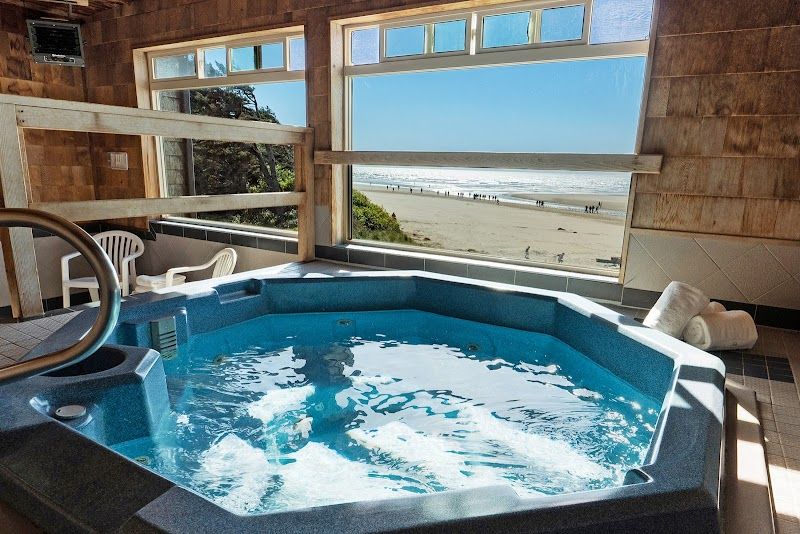 Indoor hot tub beside large windows, offering direct views of the beach and ocean shoreline